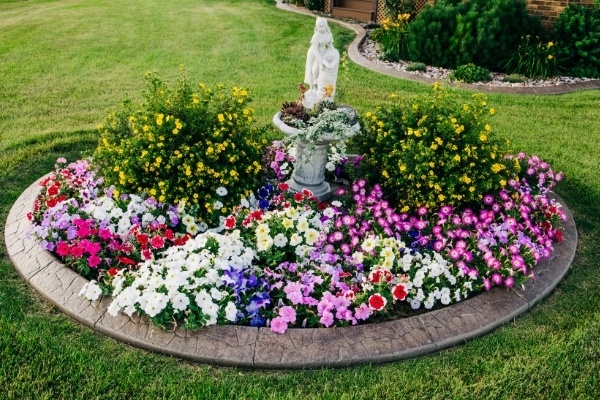 A large landscape bed filled with carefully pruned seasonal flowers and a statue.